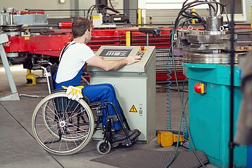Mann im Rollstuhl bedient eine Maschine in einem Betrieb.